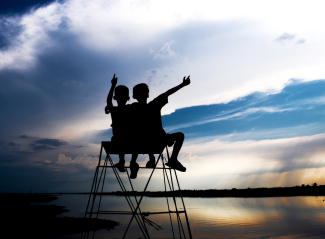 Two children silhouetted sitting in a chair looking out at the ocean